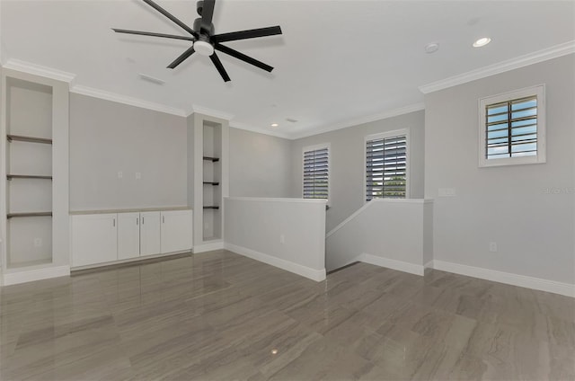 spare room with baseboards, ornamental molding, a ceiling fan, built in shelves, and wood finished floors