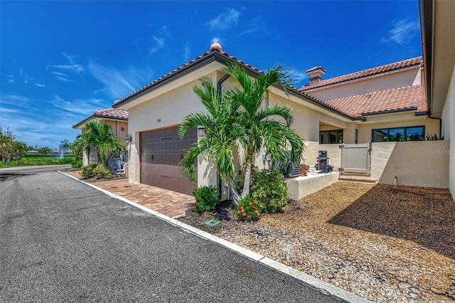 exterior space with an attached garage, stucco siding, a tile roof, and a gate
