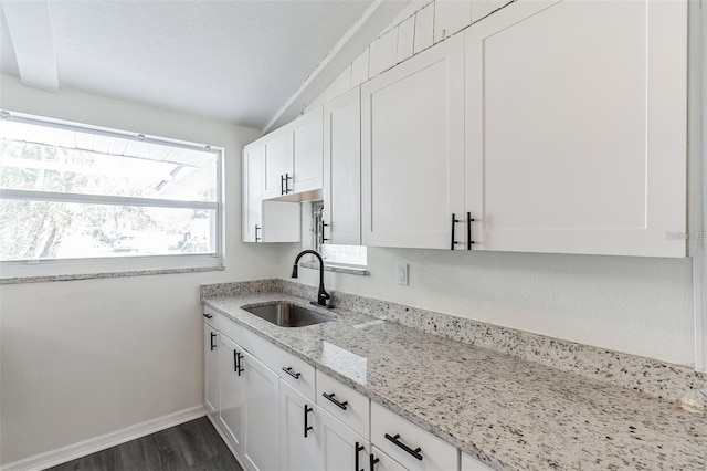 kitchen featuring white cabinets, light stone countertops, vaulted ceiling with beams, and sink