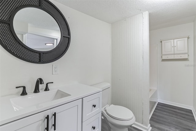 full bathroom with toilet, vanity, a textured ceiling, wood finished floors, and baseboards