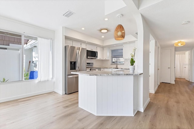 kitchen with light hardwood / wood-style flooring, pendant lighting, appliances with stainless steel finishes, kitchen peninsula, and white cabinetry