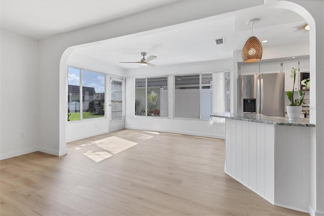 kitchen with stainless steel refrigerator with ice dispenser, light hardwood / wood-style flooring, hanging light fixtures, ceiling fan, and light stone counters