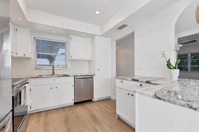 kitchen featuring light wood-type flooring, appliances with stainless steel finishes, white cabinetry, and light stone counters