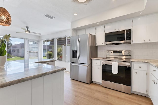 kitchen featuring white cabinets, decorative light fixtures, light stone counters, stainless steel appliances, and light hardwood / wood-style floors