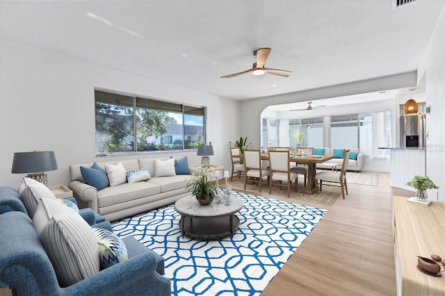 living room with light wood-type flooring, ceiling fan, and a textured ceiling