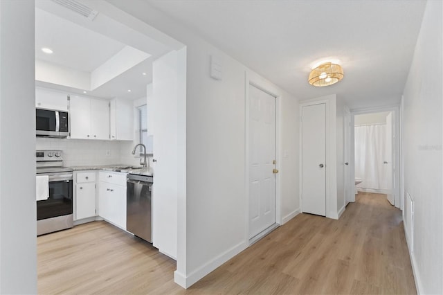 kitchen with light wood-type flooring, white cabinetry, stainless steel appliances, sink, and decorative backsplash