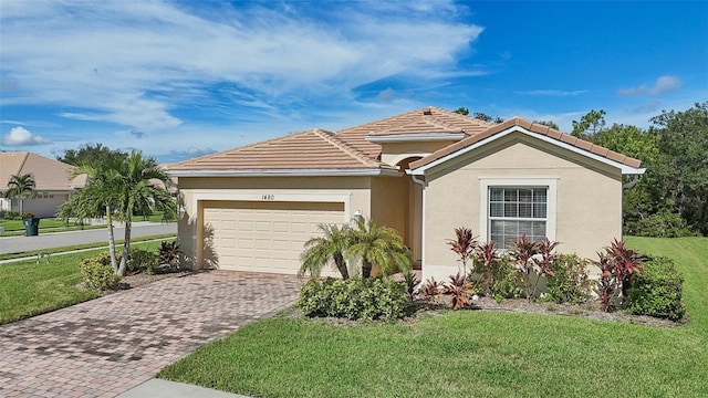 mediterranean / spanish-style home with decorative driveway, stucco siding, a front yard, a garage, and a tiled roof