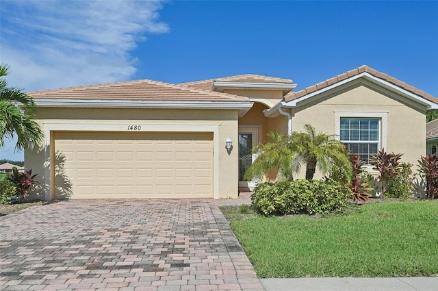 view of front of property with decorative driveway, stucco siding, a front yard, a garage, and a tiled roof