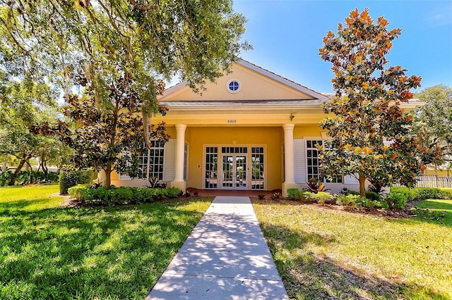 view of exterior entry featuring stucco siding, a yard, and french doors