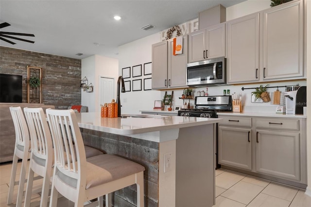 kitchen with wooden walls, gray cabinets, a kitchen island with sink, and appliances with stainless steel finishes