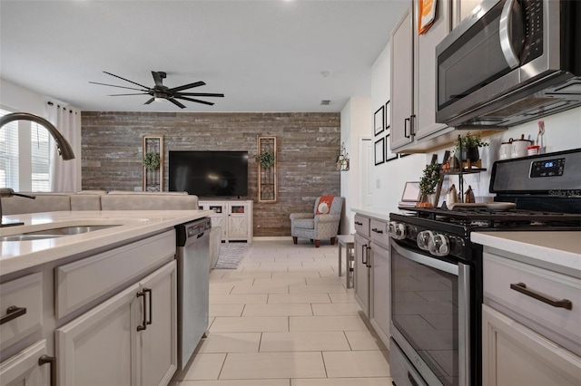 kitchen featuring ceiling fan, sink, wood walls, light tile patterned floors, and appliances with stainless steel finishes