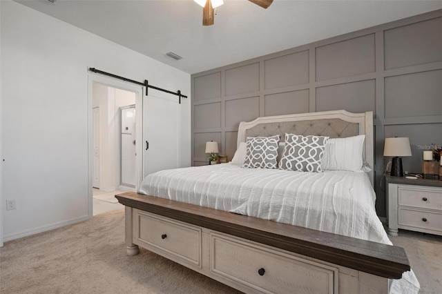 bedroom with ceiling fan, a barn door, and light colored carpet