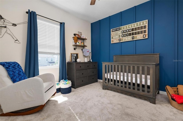 bedroom with ceiling fan, light colored carpet, and a nursery area