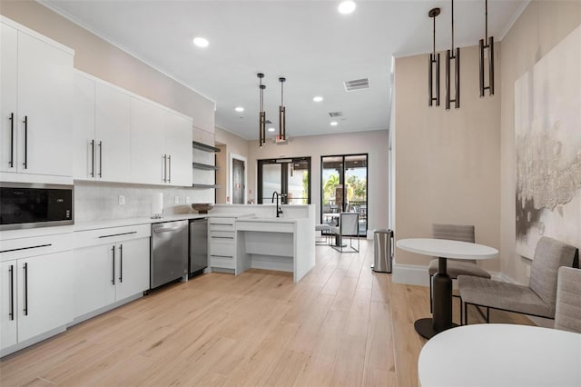 kitchen featuring kitchen peninsula, tasteful backsplash, built in microwave, pendant lighting, and white cabinets