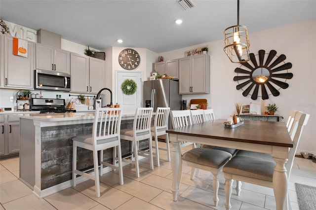 kitchen with appliances with stainless steel finishes, light tile patterned floors, gray cabinets, hanging light fixtures, and an island with sink