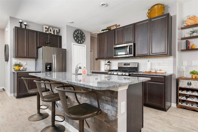 kitchen with appliances with stainless steel finishes, backsplash, and a center island with sink