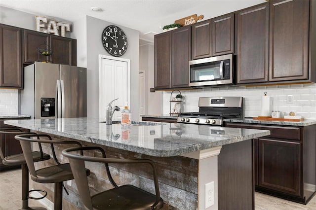 kitchen featuring a kitchen island with sink, appliances with stainless steel finishes, and a kitchen bar