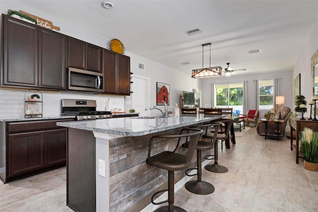 kitchen featuring hanging light fixtures, backsplash, appliances with stainless steel finishes, sink, and a kitchen island with sink