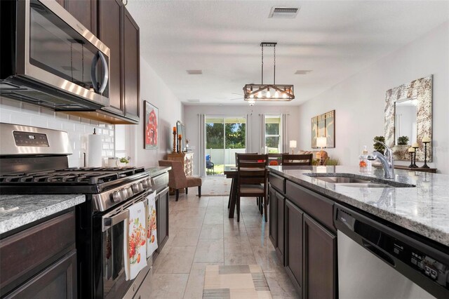 kitchen featuring appliances with stainless steel finishes, pendant lighting, light stone countertops, and sink