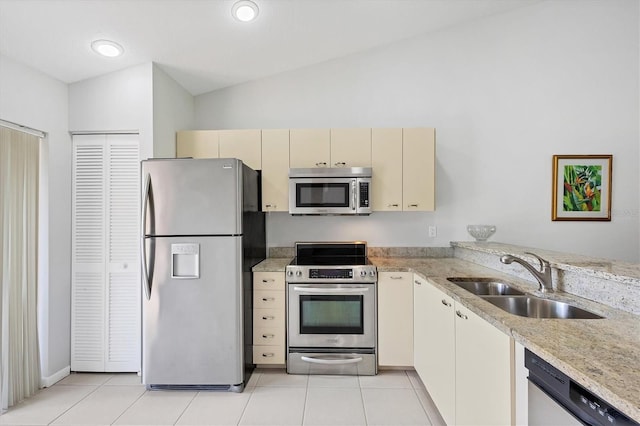 kitchen with cream cabinets, sink, vaulted ceiling, light tile patterned floors, and appliances with stainless steel finishes