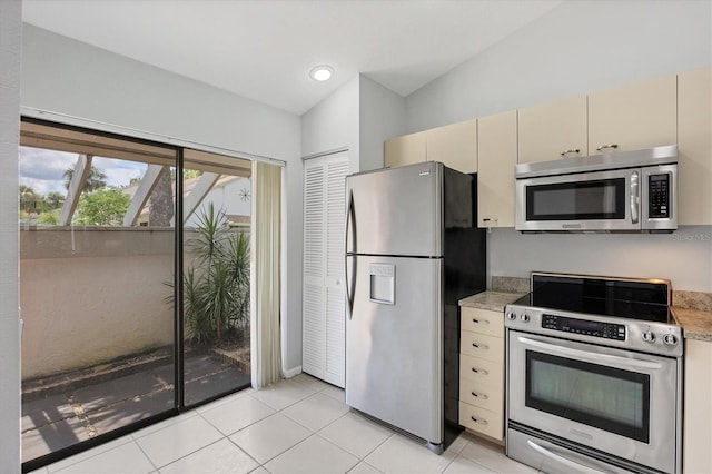 kitchen featuring light tile patterned floors, stainless steel appliances, cream cabinets, and vaulted ceiling