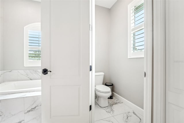 bathroom featuring tiled bath and toilet