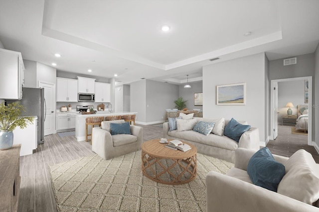 living room with light wood-type flooring, a tray ceiling, and sink