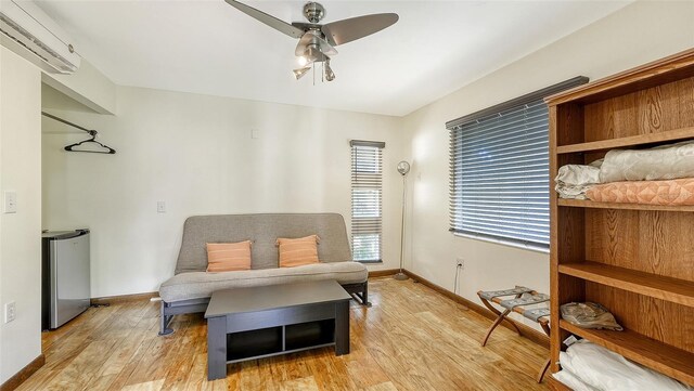 living area with ceiling fan, an AC wall unit, and light hardwood / wood-style flooring