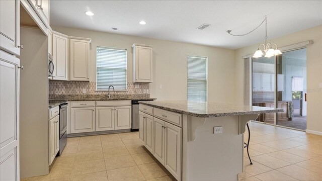 kitchen with pendant lighting, a kitchen island, an inviting chandelier, sink, and stone countertops