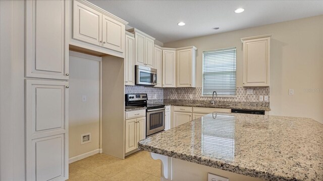 kitchen with light stone counters, stainless steel appliances, sink, light tile patterned flooring, and decorative backsplash