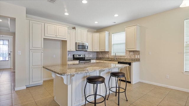 kitchen featuring a center island, appliances with stainless steel finishes, light stone counters, a kitchen breakfast bar, and tasteful backsplash