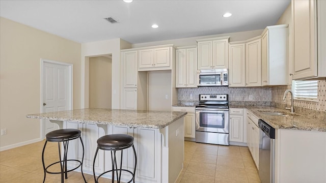 kitchen with a kitchen island, stainless steel appliances, sink, and light stone countertops