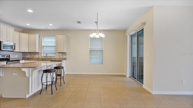 kitchen featuring a notable chandelier, tasteful backsplash, light stone counters, appliances with stainless steel finishes, and a breakfast bar area