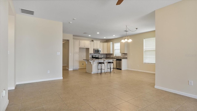 kitchen with ceiling fan with notable chandelier, stainless steel appliances, a kitchen breakfast bar, a kitchen island, and tasteful backsplash