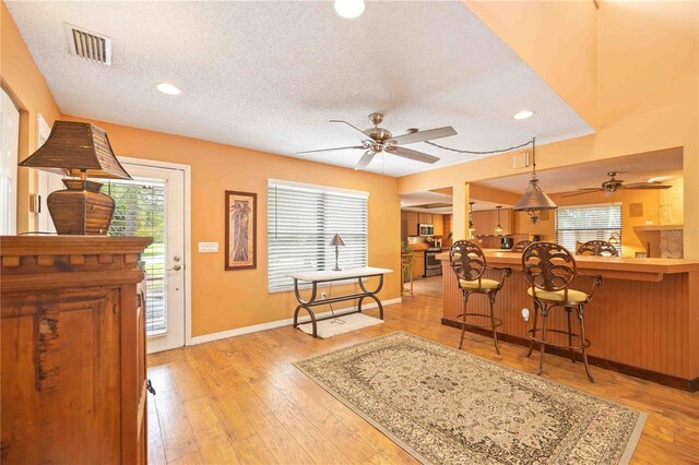 living room featuring light wood-type flooring, ceiling fan, bar, and a textured ceiling