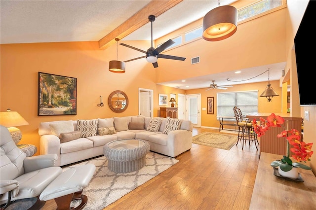 living room featuring a textured ceiling, beamed ceiling, light hardwood / wood-style floors, high vaulted ceiling, and ceiling fan