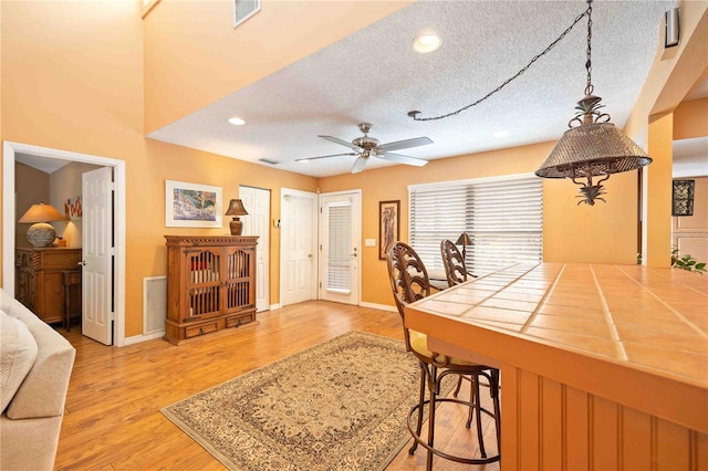 kitchen with a textured ceiling, light hardwood / wood-style flooring, tile counters, a kitchen bar, and ceiling fan