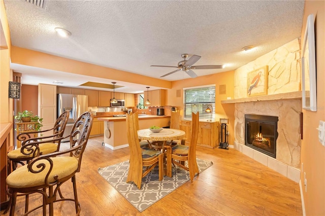 dining space with light wood-type flooring, a textured ceiling, ceiling fan, and a stone fireplace