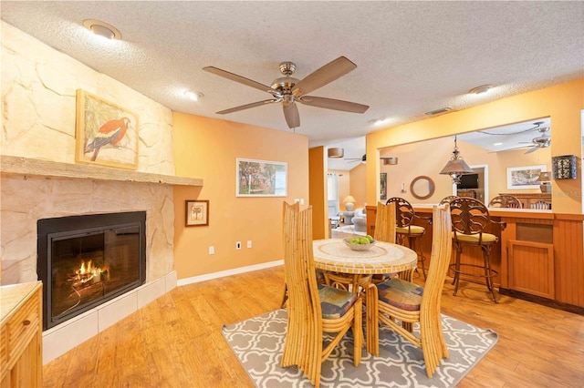 dining space with light wood-type flooring, ceiling fan, a fireplace, and a textured ceiling