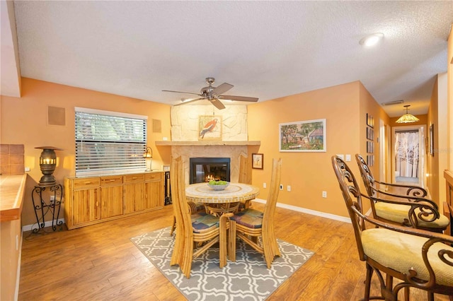 dining space featuring a fireplace, a textured ceiling, light hardwood / wood-style flooring, and ceiling fan