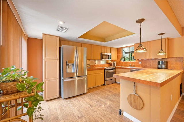 kitchen featuring pendant lighting, kitchen peninsula, light wood-type flooring, and appliances with stainless steel finishes