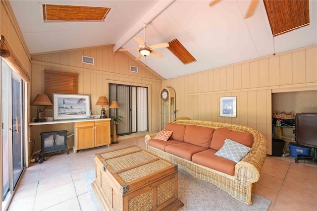 living room with a wood stove, light tile patterned floors, ceiling fan, and vaulted ceiling with beams