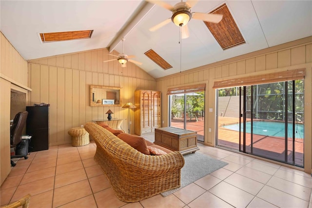 interior space with vaulted ceiling with skylight, ceiling fan, and wooden walls