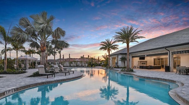 pool at dusk with a gazebo, a patio, and a community pool