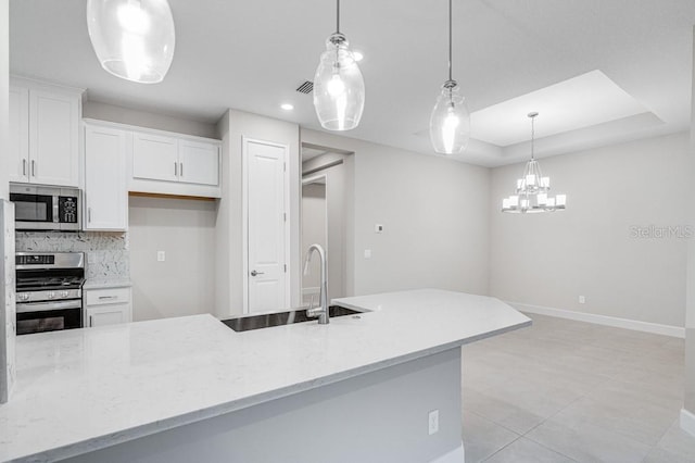 kitchen featuring a raised ceiling, backsplash, appliances with stainless steel finishes, white cabinetry, and light stone countertops