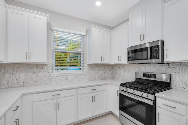 kitchen featuring appliances with stainless steel finishes, white cabinetry, decorative backsplash, and light stone counters