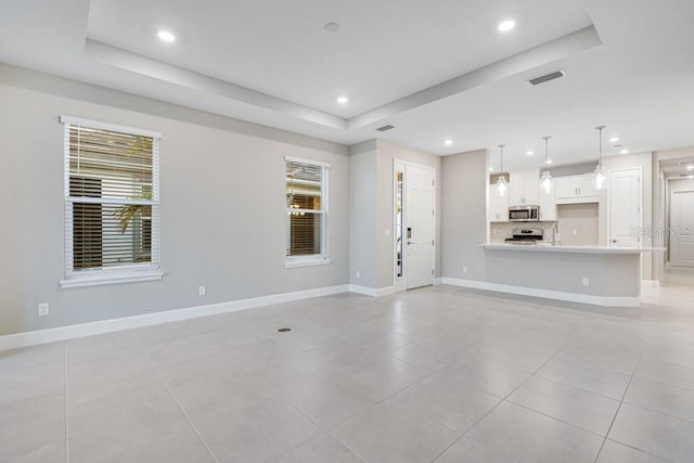 unfurnished living room featuring baseboards, visible vents, a raised ceiling, and recessed lighting