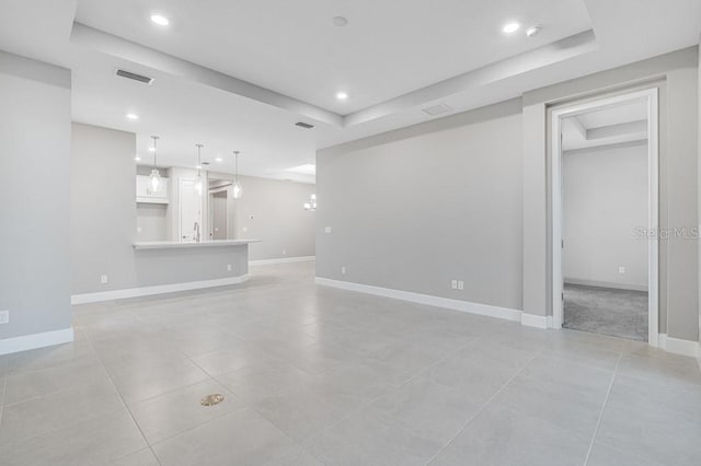 unfurnished living room featuring a raised ceiling, visible vents, and baseboards