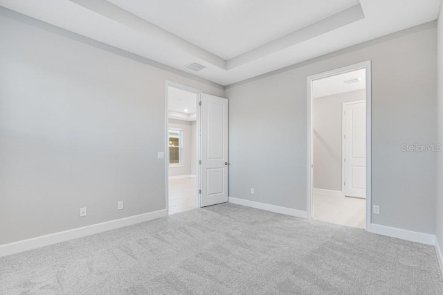 spare room with visible vents, baseboards, a raised ceiling, and light colored carpet