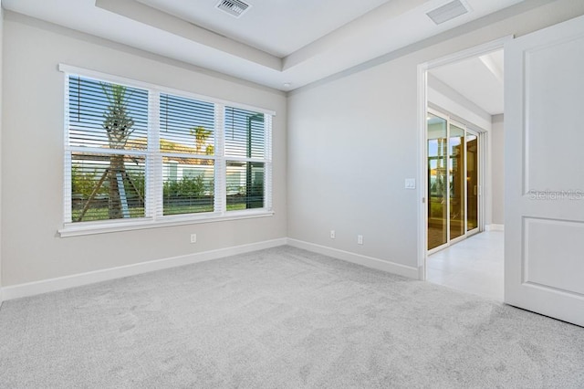 unfurnished room with a tray ceiling, carpet flooring, visible vents, and baseboards